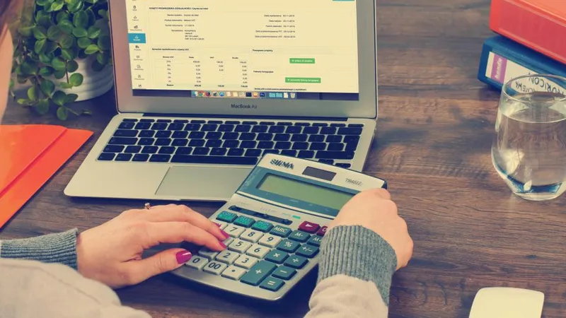 Puesto de trabajo administrativo: manos operando una calculadora junto a una computadora con una planilla